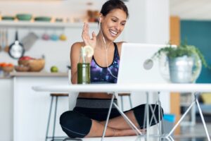 Shot of sporty beautiful woman having an online video call via laptop computer while drinking detox juice in the kitchen at home.